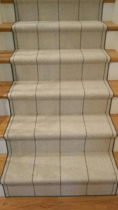 Carpeted stairs with a cream-colored, patterned runner with black and red stripes.