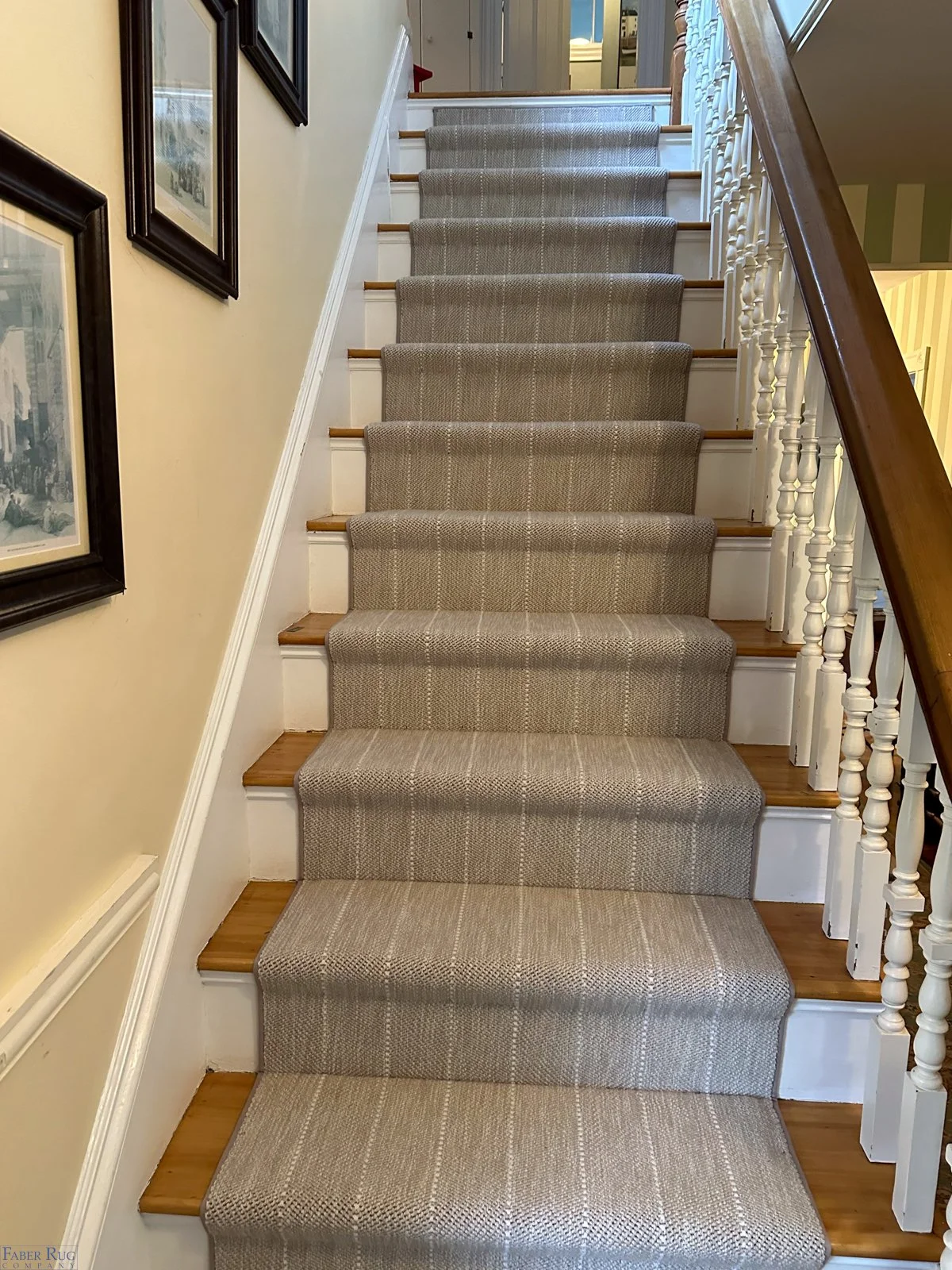 Indoor staircase with tan carpet runner, wooden steps, white risers, and a wooden handrail, decorated with framed pictures on a yellow wall.