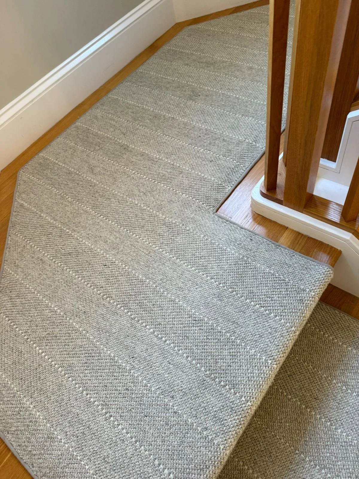 Close-up of a beige runner rug with a subtle striped pattern on a hardwood staircase landing with wooden railing.