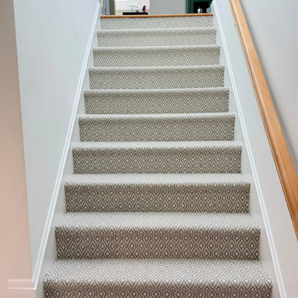 Carpeted staircase viewed from bottom up, with a patterned beige and brown rug.
