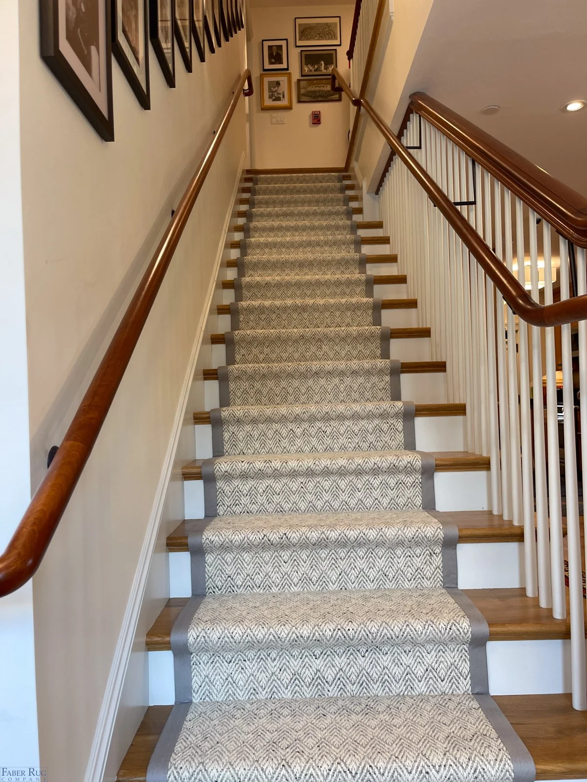 Indoor staircase with beige patterned carpet runner, wooden handrails, and framed artwork on the wall.