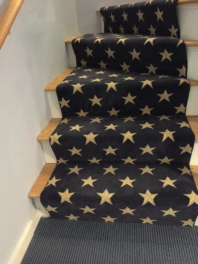 Carpeted staircase with black runner featuring white stars, extending from the top step down to the floor.