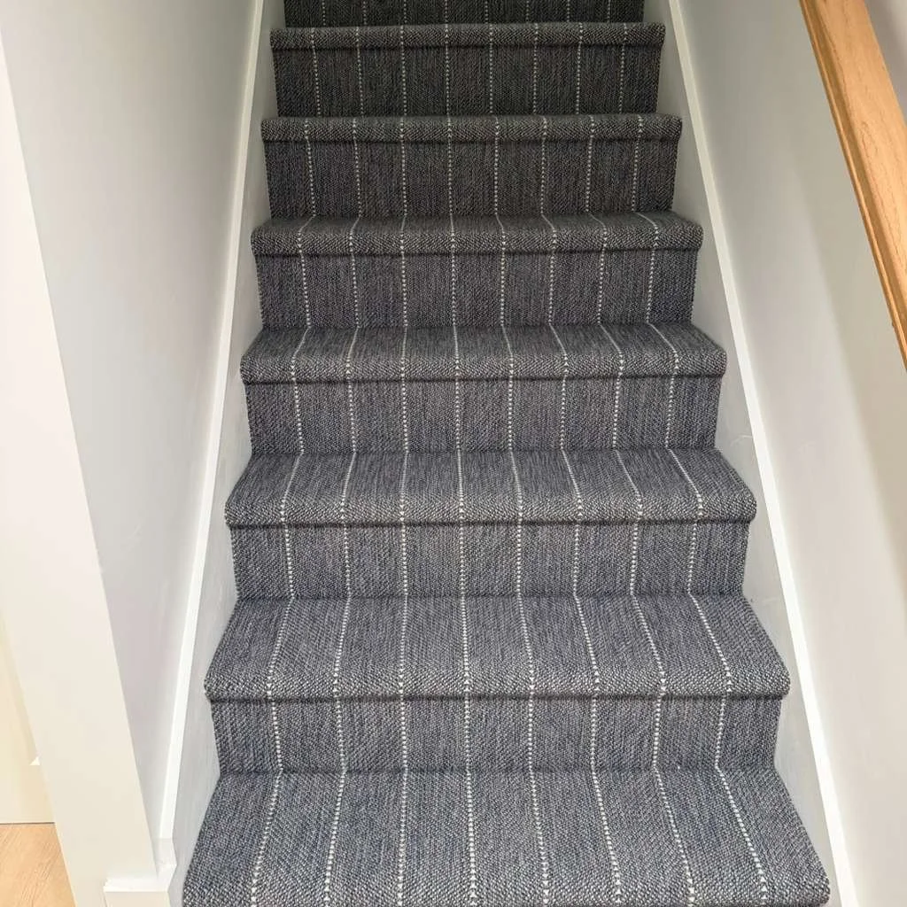 A staircase with gray carpet featuring white plaid stripes in a residential home.