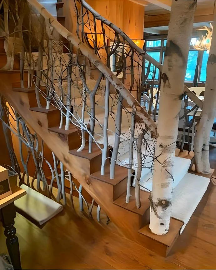 Wooden staircase with metal and branch-like handrails, integrated into a decor featuring birch trees and natural wood elements.