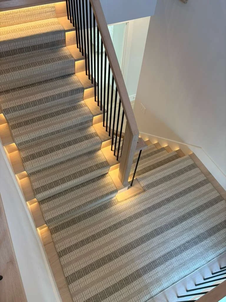 Indoor lighted staircase with striped carpet runner and built-in lighting along the steps.