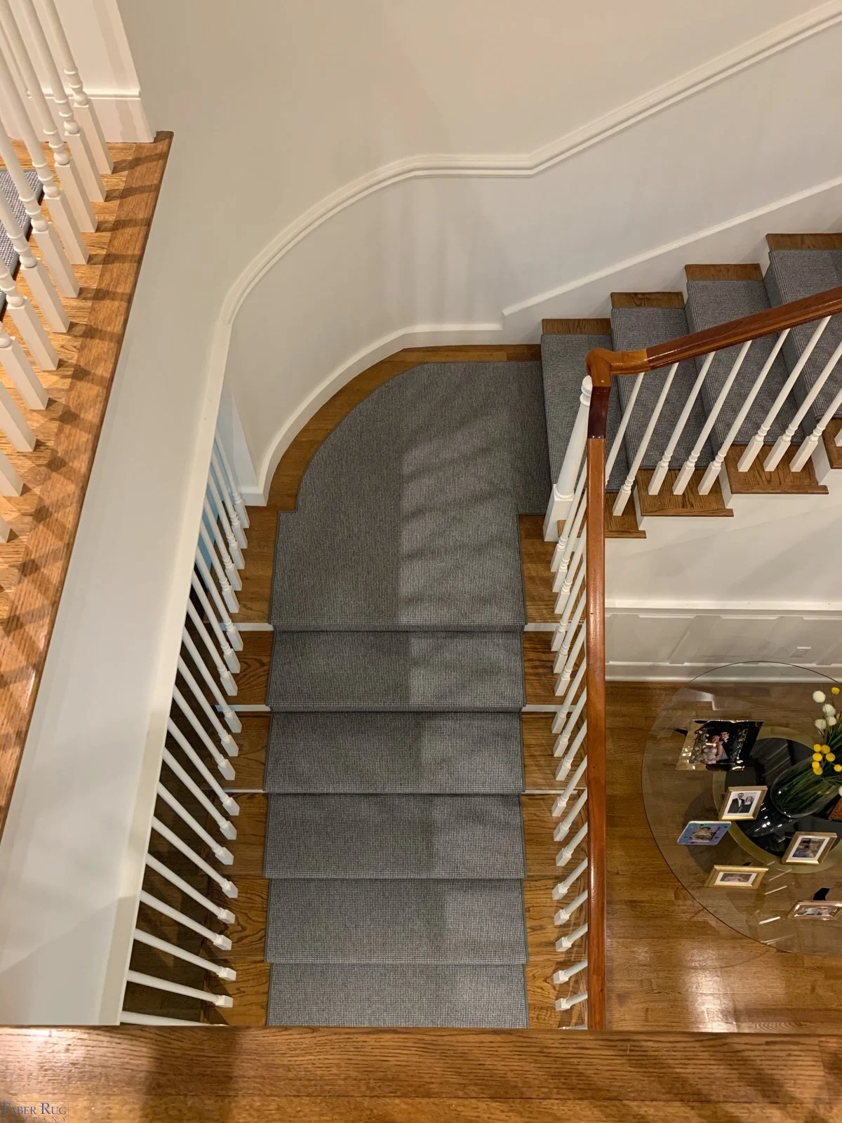 Indoor staircase with gray carpeted steps, wooden handrail, white spindles, and a curved wall.