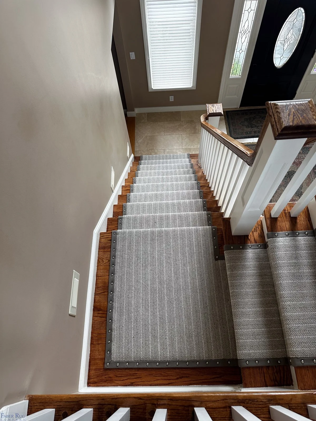 View of a staircase from above, showing beige carpet with metal edge inserts, wooden handrails, and a front door with a decorative glass window in a home.