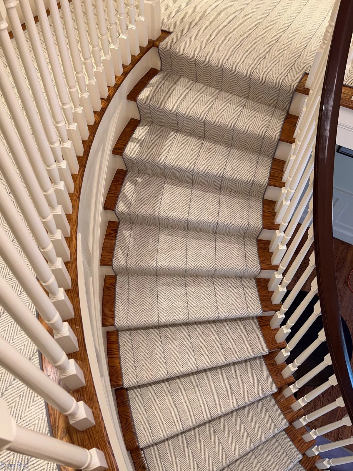 Overhead view of a curved staircase with white spindles, wooden steps, and beige patterned carpet.