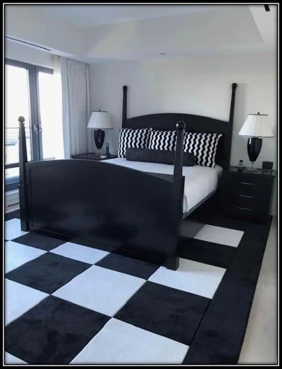A black wooden bed with black and white striped bedding, two matching bedside lamps, and a black and white checkered rug in a modern bedroom.