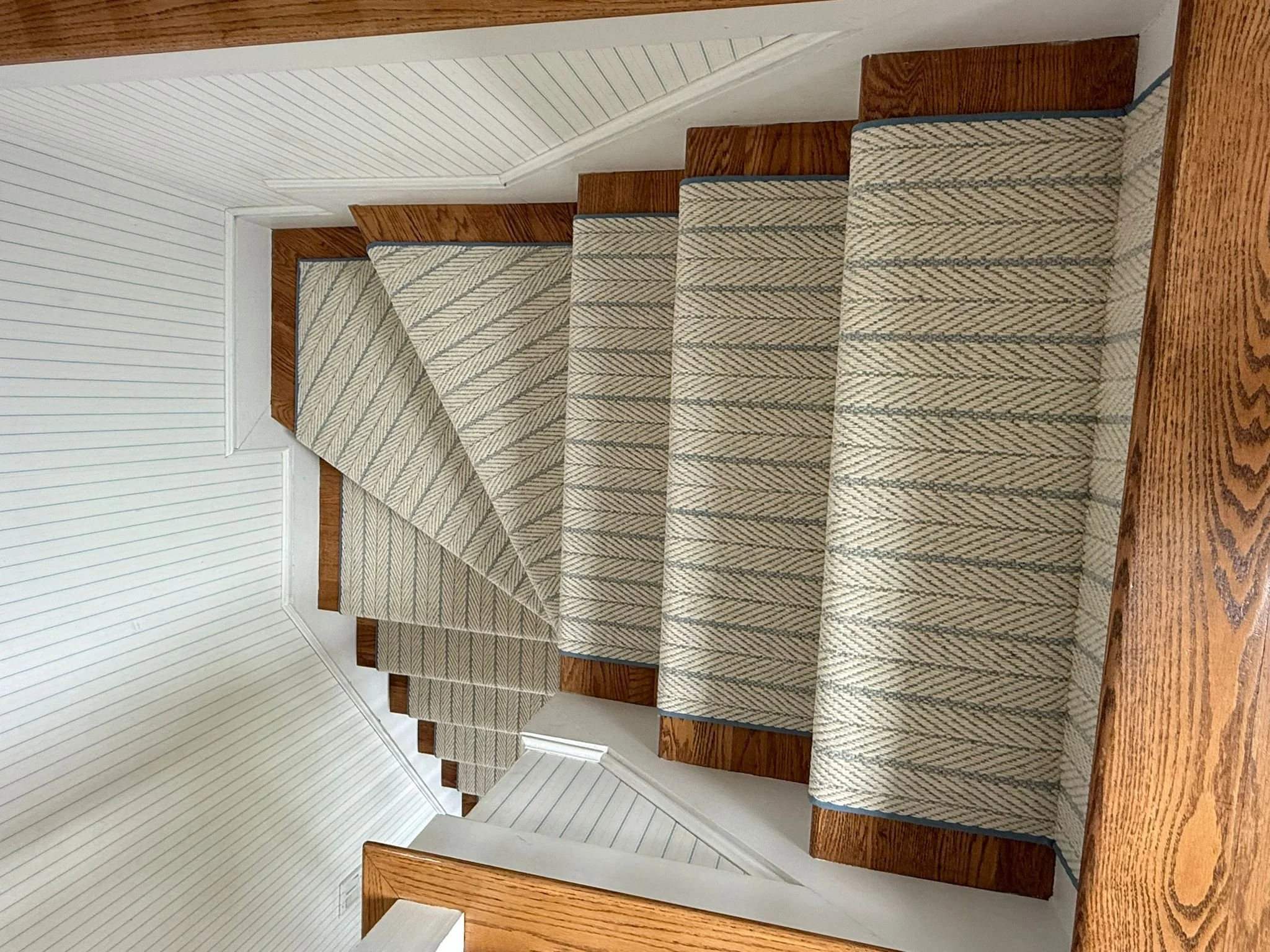 Carpeted staircase with a beige and blue chevron pattern, wooden steps, and white paneled walls.
