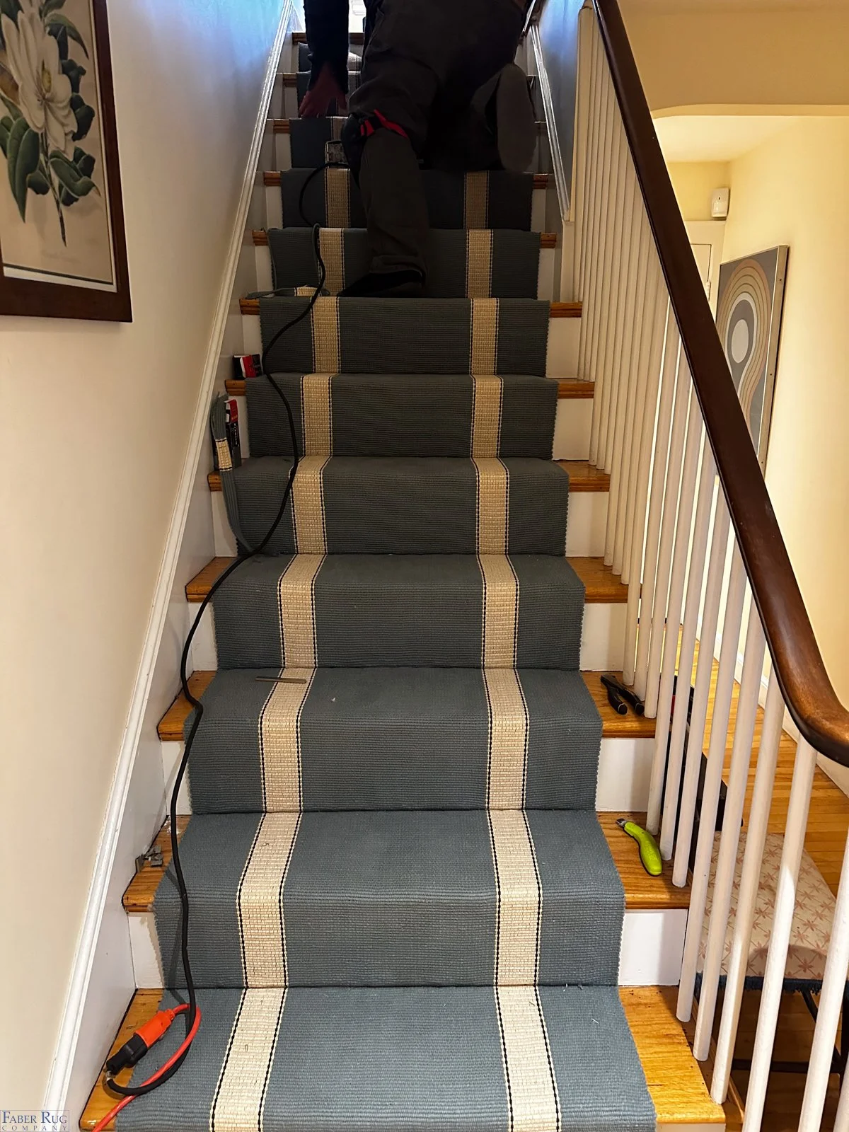 Staircase with a gray striped runner and tools on the steps, including a cord with a plug and small hand tools, leading upstairs in a home.