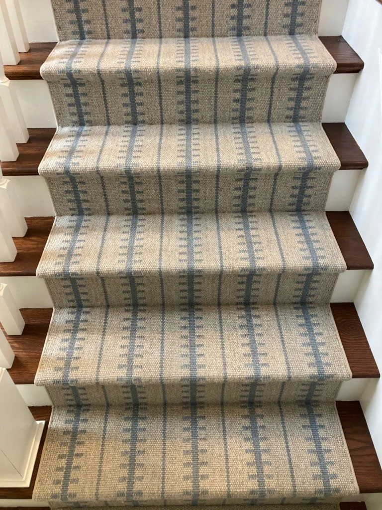 Carpeted staircase with a gray and beige striped pattern, with dark brown wooden steps on either side and white risers.