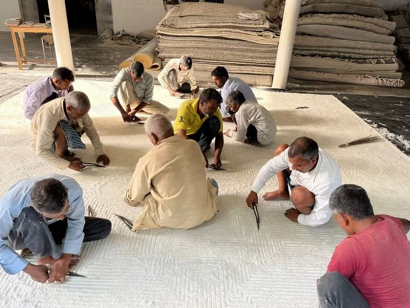 Artisans, indigenous to India, crouched, sitting, and hand carving a hand knotted wool rug. Custom 100% wool area rug (carpet, oriental) for a Faber Rug Customer.