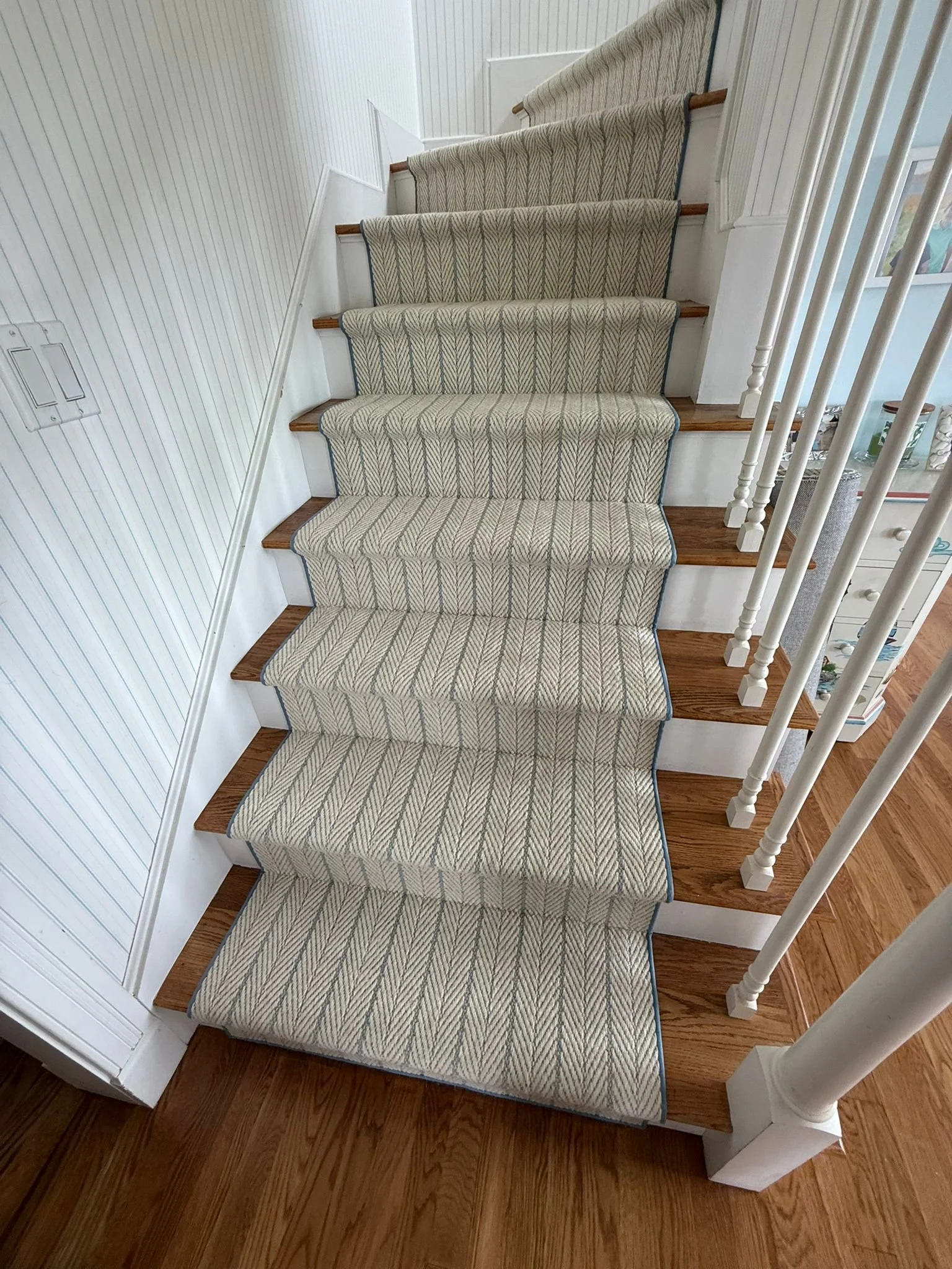 Carpeted staircase with a herringbone pattern, white risers, wooden treads, white walls, and a white railing.