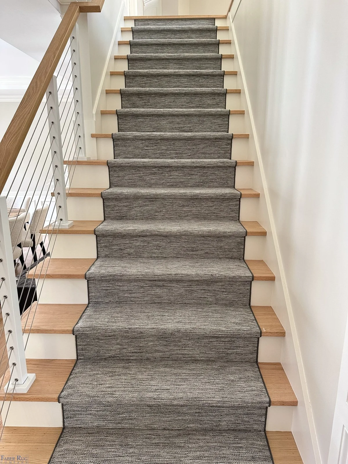 Indoor staircase with gray carpeted steps, wooden treads, white risers, and a modern metal railing on the left side.