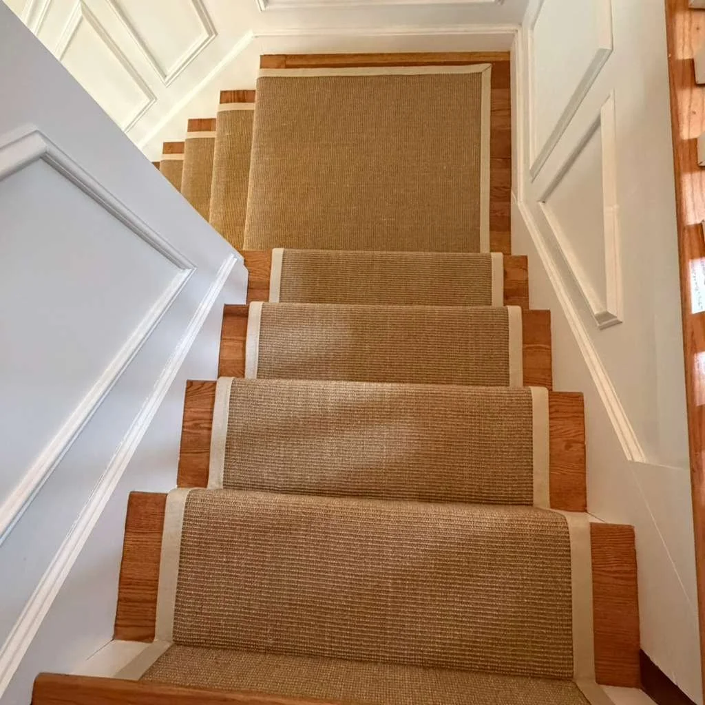 Sisal carpet flowing down a flight of stairs New York Style with miters on the corners and wide binding.
