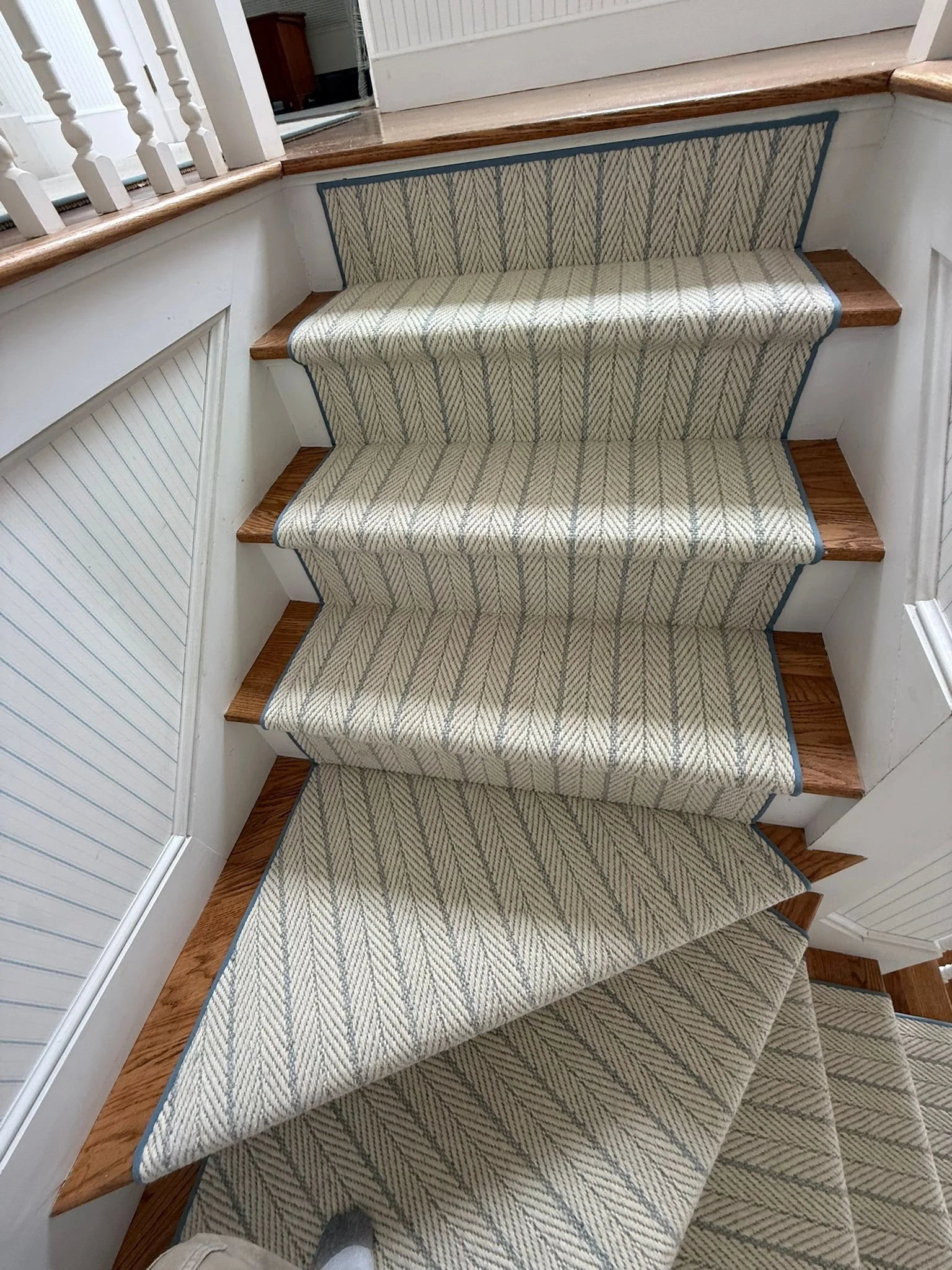 Carpeted staircase with a light-colored, striped pattern and wooden steps with a blue trim at the edge.