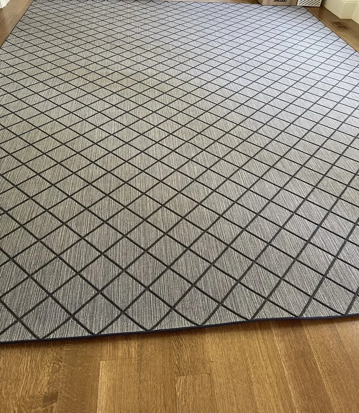 Rectangular area rug with a geometric diamond pattern in black and gray on a wooden floor.