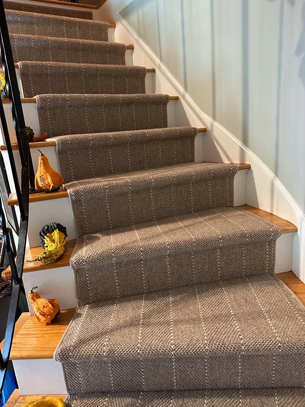 Carpeted staircase with a brown patterned runner, small decorative pumpkins and gourds on the stairs, and a black metal railing on the left.