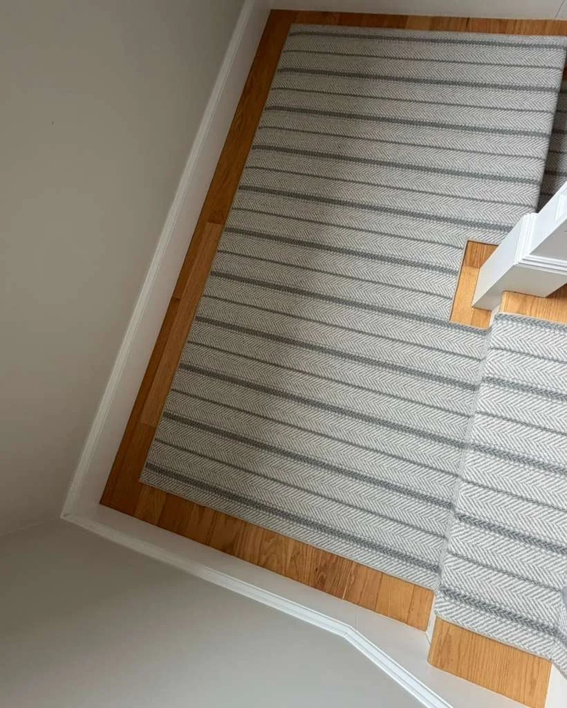 Top-down view of a hallway corner with a striped area rug on a hardwood floor and white wall.