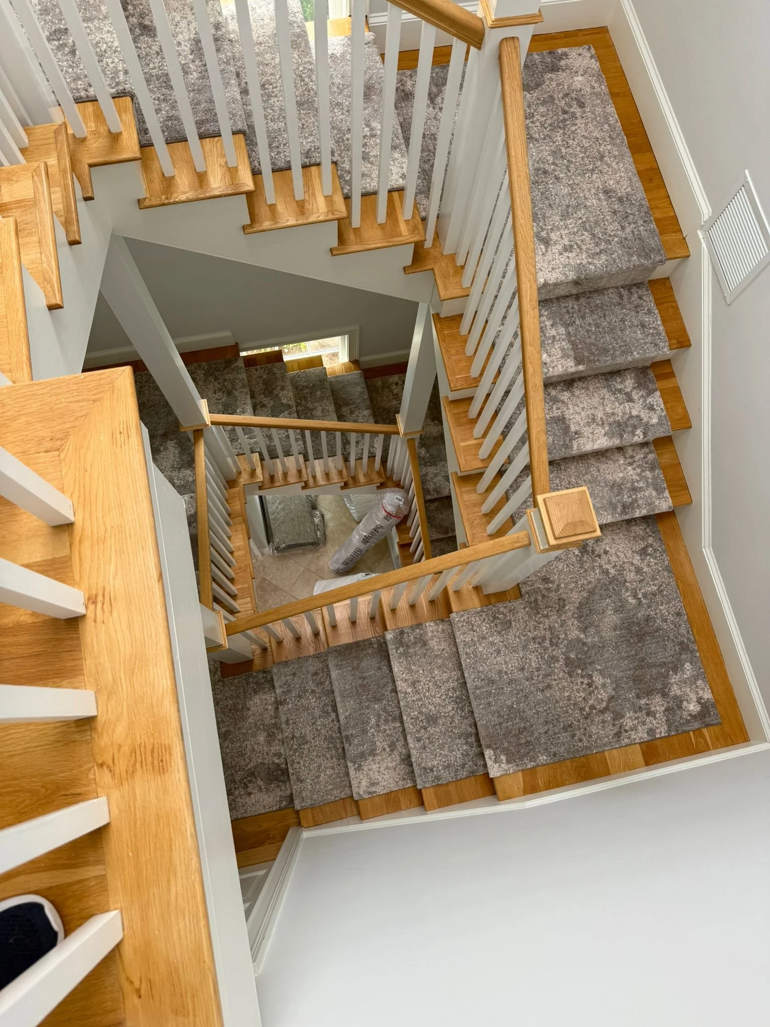 A view looking down a staircase with wooden steps, white railings, and gray carpeted treads, showing multiple levels in a house.