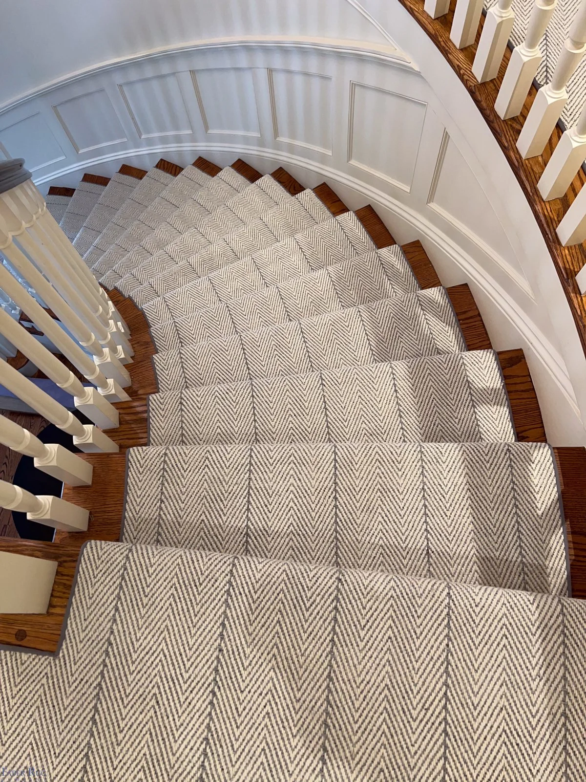 View of curved staircase with patterned carpet, white spindles, and wooden handrail.