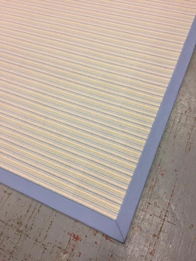 Close-up of a striped area rug with a solid blue border, on a wooden floor.