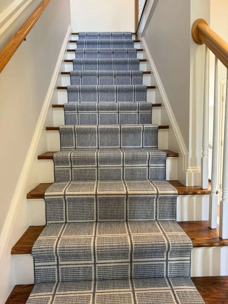Indoor stairs with a gray and white checkered runner rug and wooden handrails.