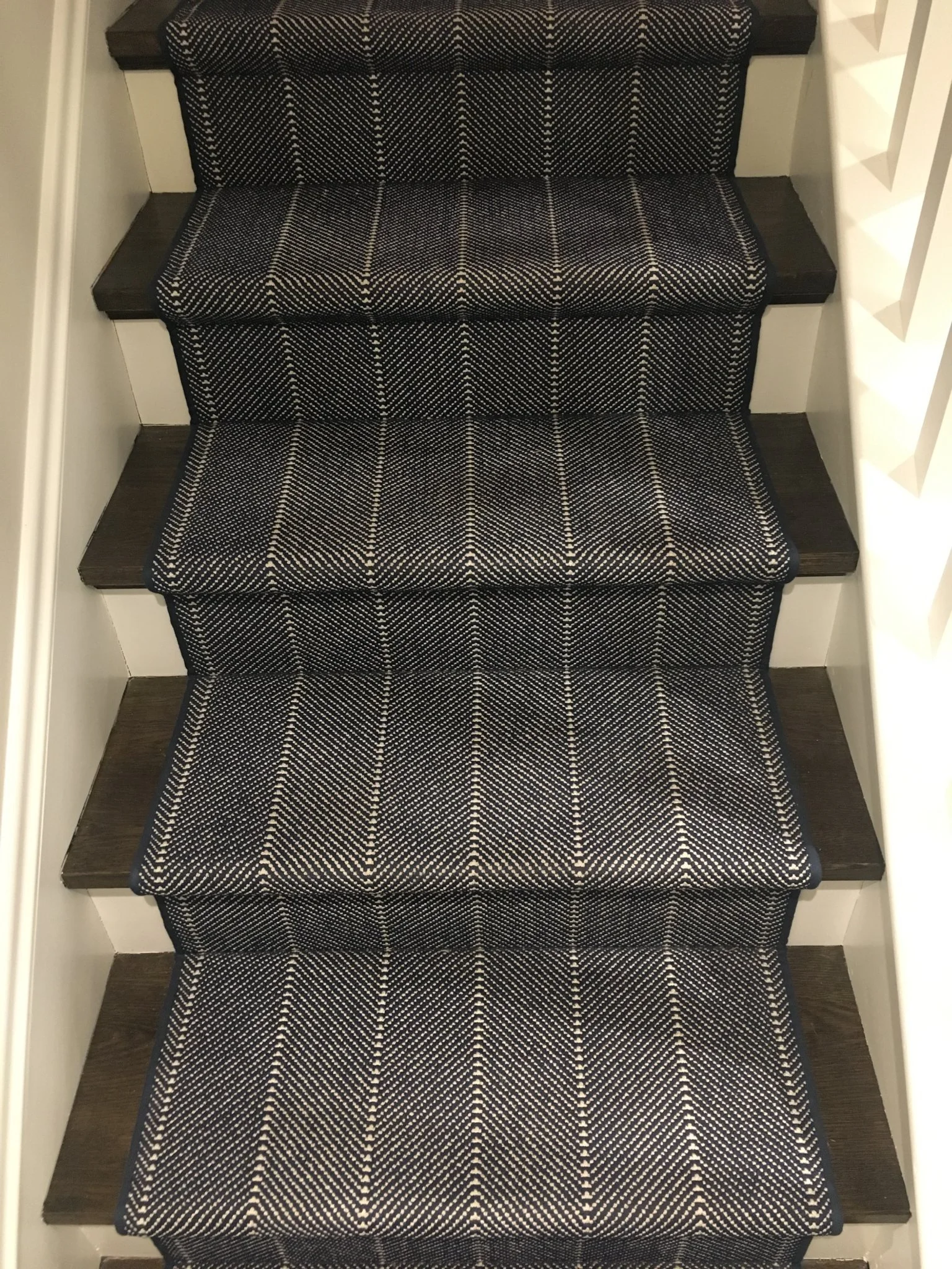 Carpeted stairs with a dark geometric pattern, with dark wooden steps and white risers, on a staircase.