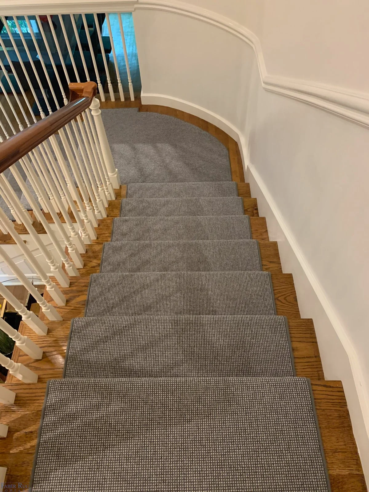Indoor staircase with gray carpeting, wooden steps, white spindles, and a curved wooden handrail.