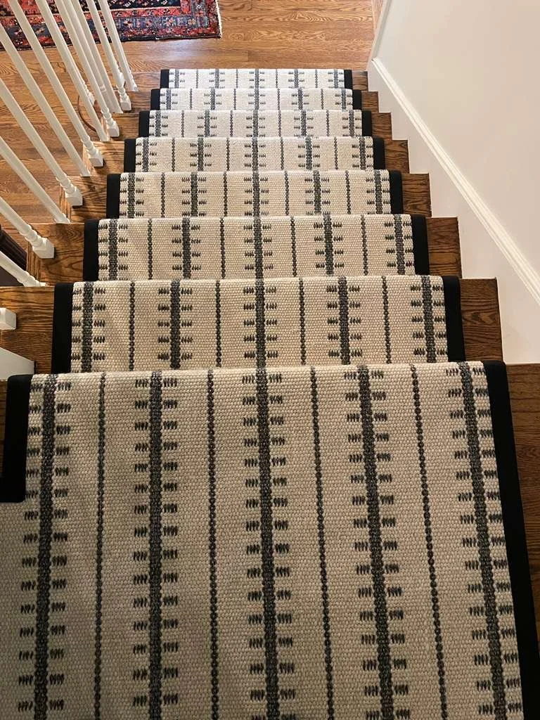 Staircase with a patterned runner carpet, wooden steps, white railings on the left, and a hardwood floor at the top.