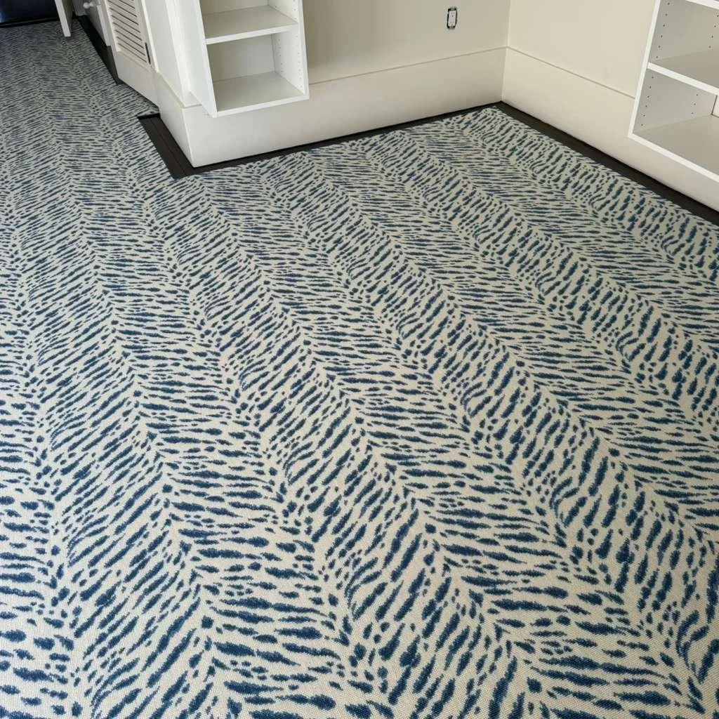Close-up of a patterned carpet with blue and white streaks in a room with white walls and built-in shelves.