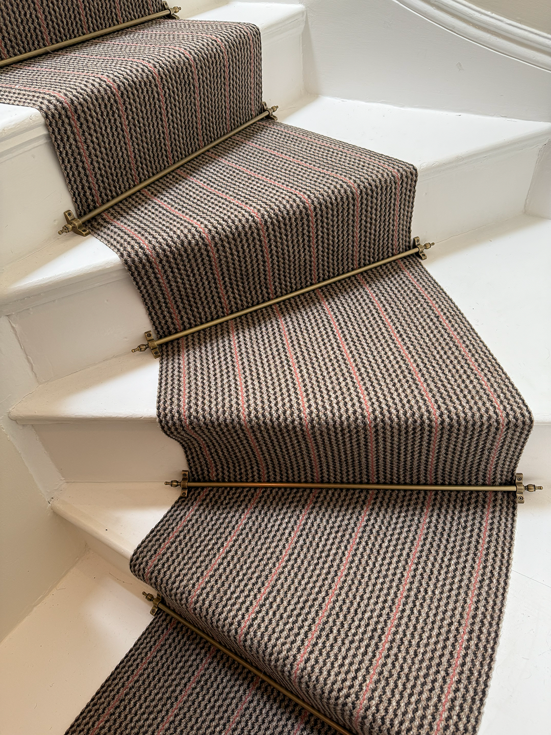 A staircase with a patterned runner carpet, held in place by brass stair rods.