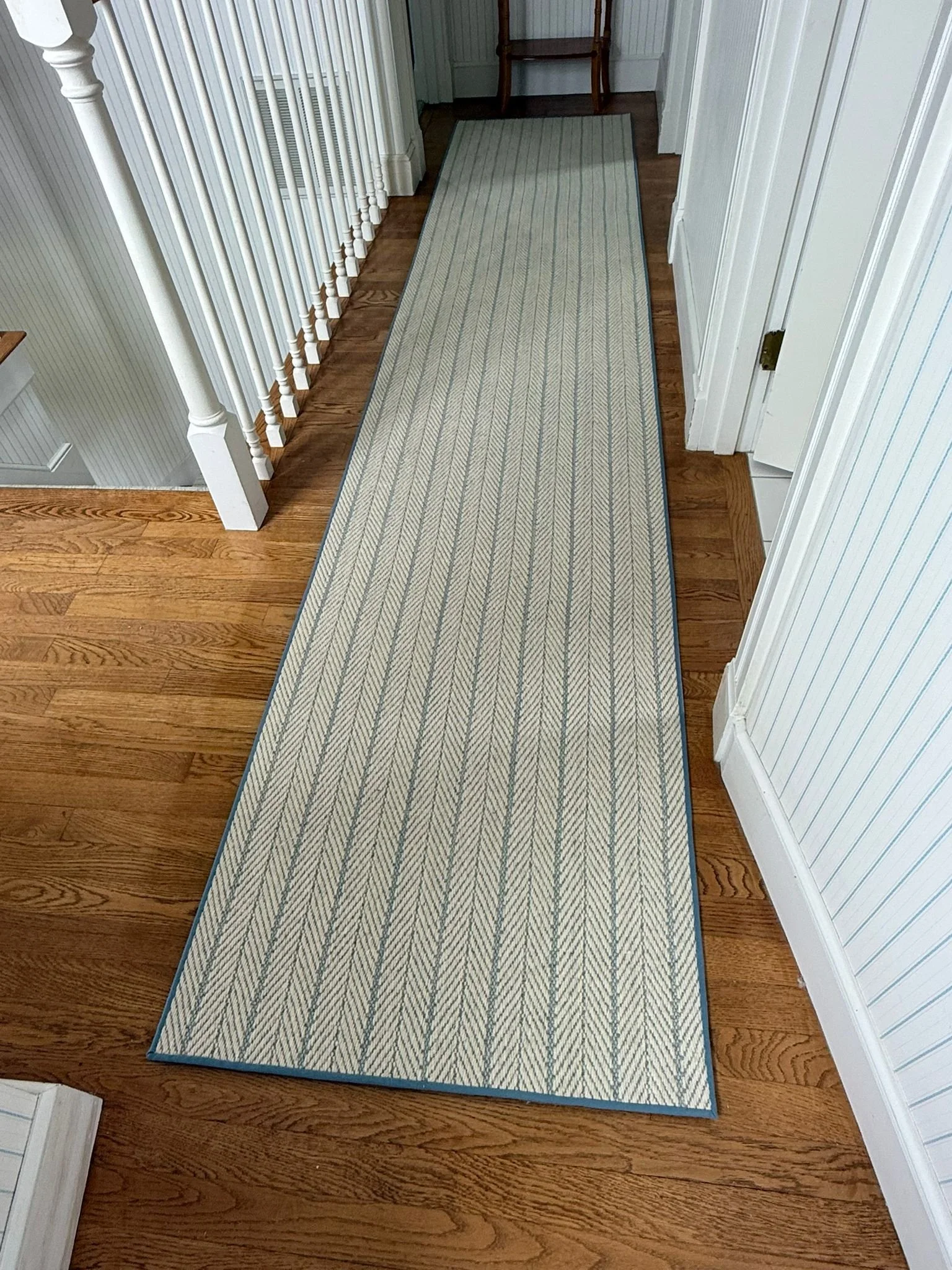 A long, rectangular beige area rug with blue border and diagonal stripe pattern on a hardwood floor in a hallway.