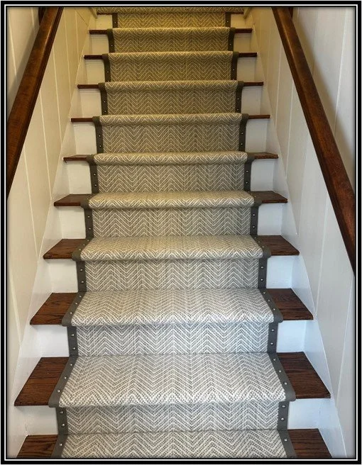Carpeted staircase with wooden steps on the sides and dark handrails.