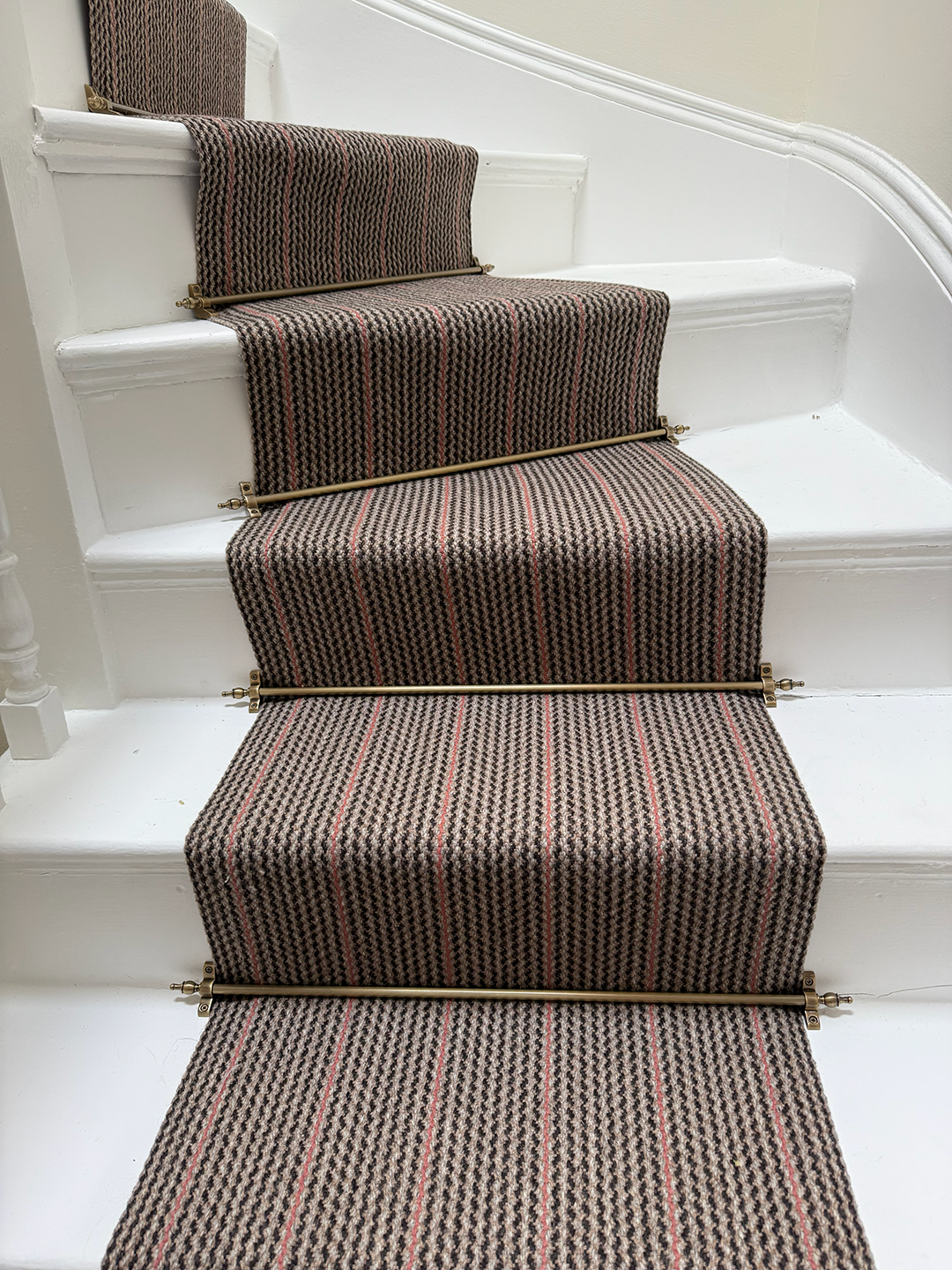 A staircase with a patterned carpet runner, installed with metal stair rods, on white-painted steps and risers.