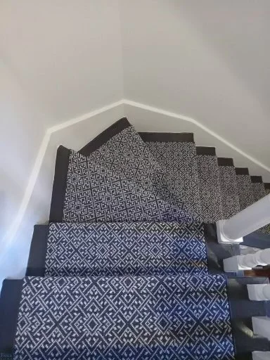 Top view of a staircase with a patterned runner carpet, white walls, and a black ledge at the staircase edge.