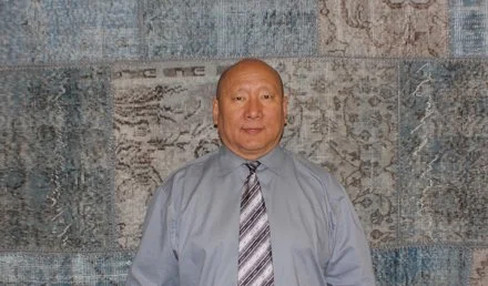 Jampa in a light gray dress shirt and striped tie standing in front of a patchwork rug background Faber Rug @faberrug.
