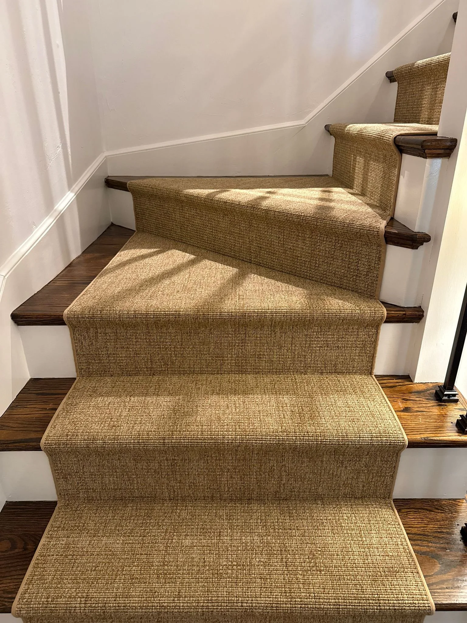 Indoor staircase with four carpeted steps, each with a different pattern and color, bordered by wooden trim, leading up to a white wall.