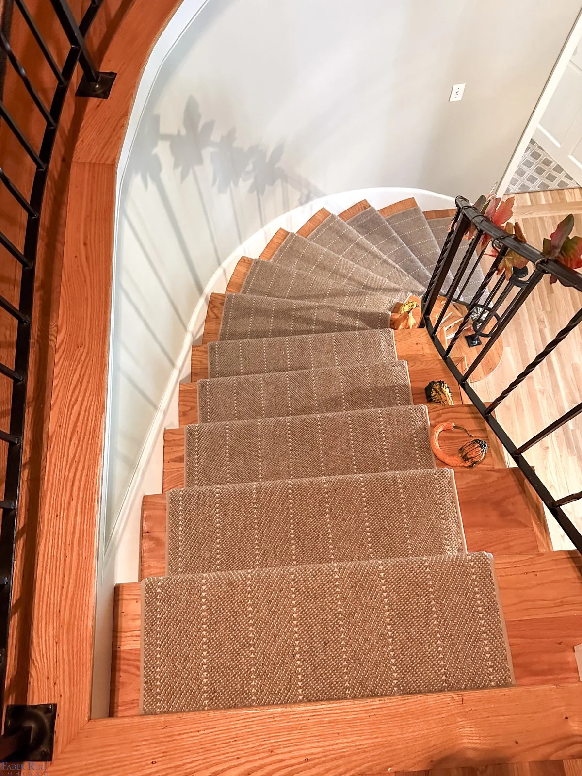 Top view of a spiral staircase with brown carpeted steps, black metal handrail, and decorative fall leaves and pumpkin accents on the railing.