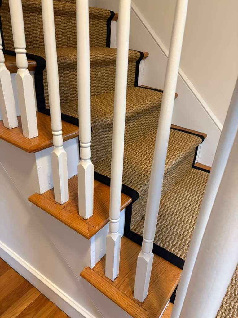 Wooden staircase with beige carpeted steps and white railing spindles.