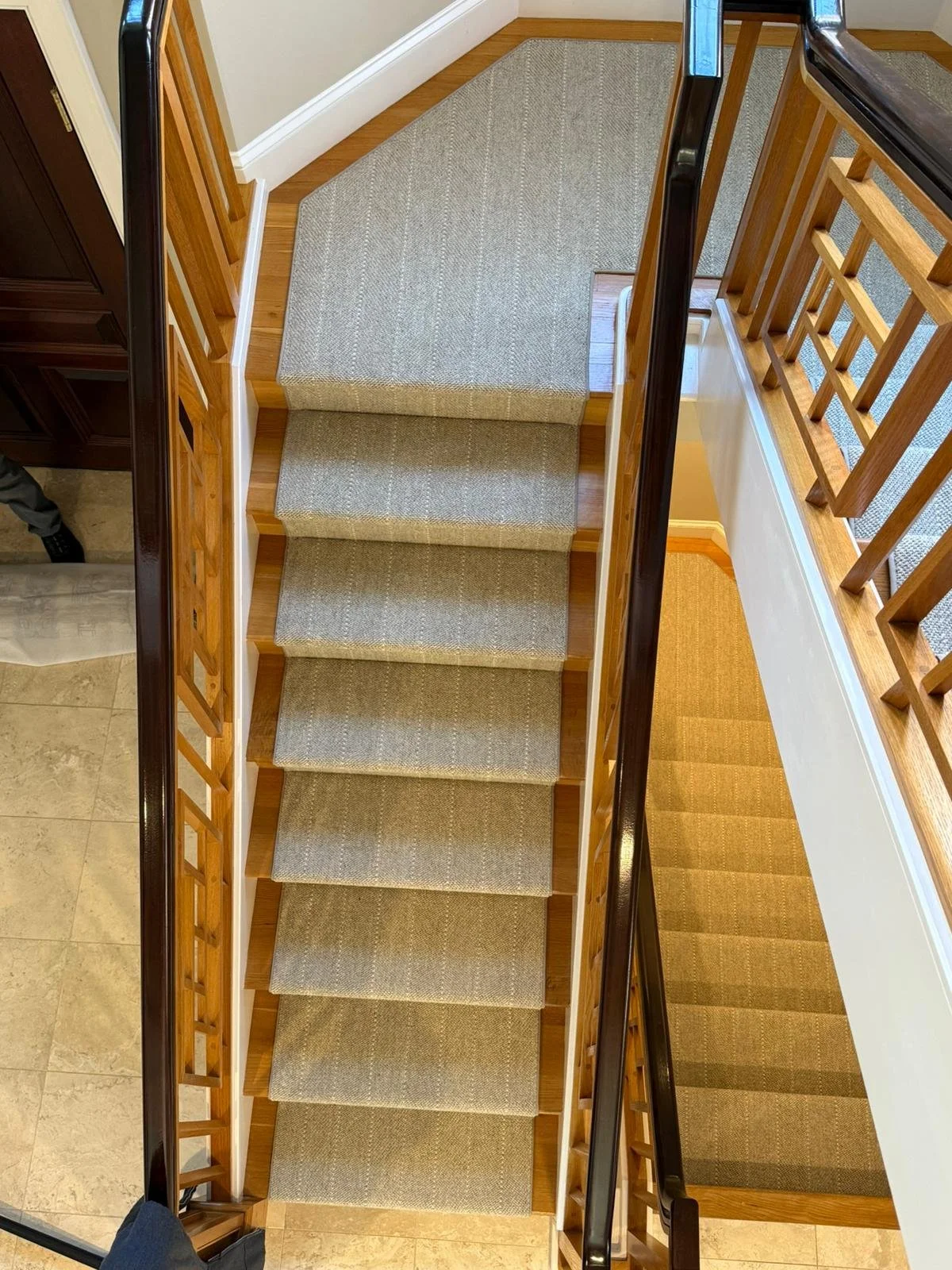 Top-down view of a staircase with carpeted steps, wooden railings, and a landing at the top, with carpeted flooring surrounding the staircase.