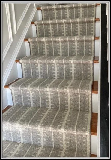 Carpeted staircase with striped beige and gray pattern and wooden handrails.