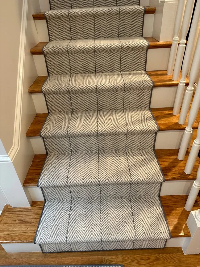 Carpeted stairs with a runner in a plaid pattern, bordered by wooden steps and white railings.