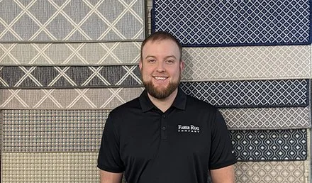 Ryan Smiling in black polo shirt standing in front of a display of various patterned carpets or rugs on wall @faberrug.