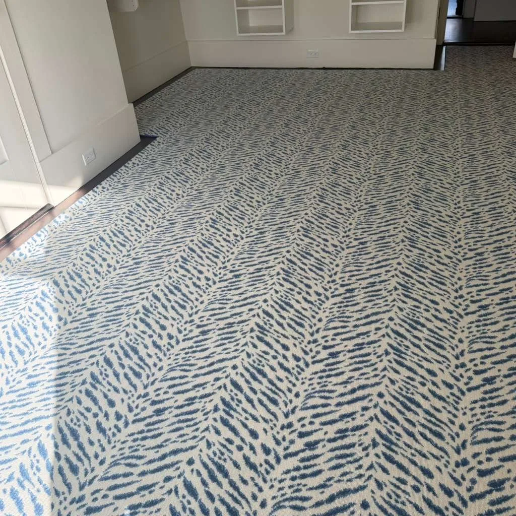 Close-up of a carpet with a blue and white abstract animal print pattern in a room with white walls and built-in shelves.