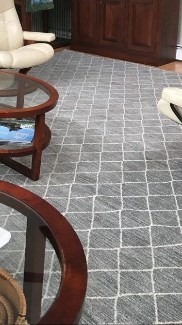 Living room with a grey patterned rug, white armchairs, and wooden furniture.