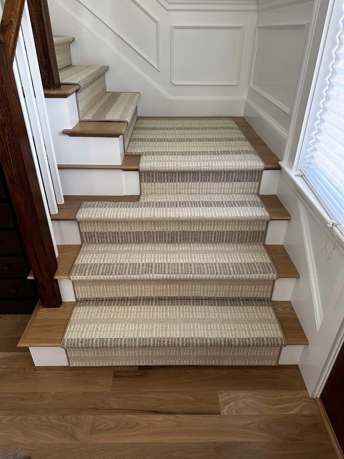 Carpeted staircase with six steps, beige and brown striped carpet, wooden treads, white risers, and a window with blinds on the right side.