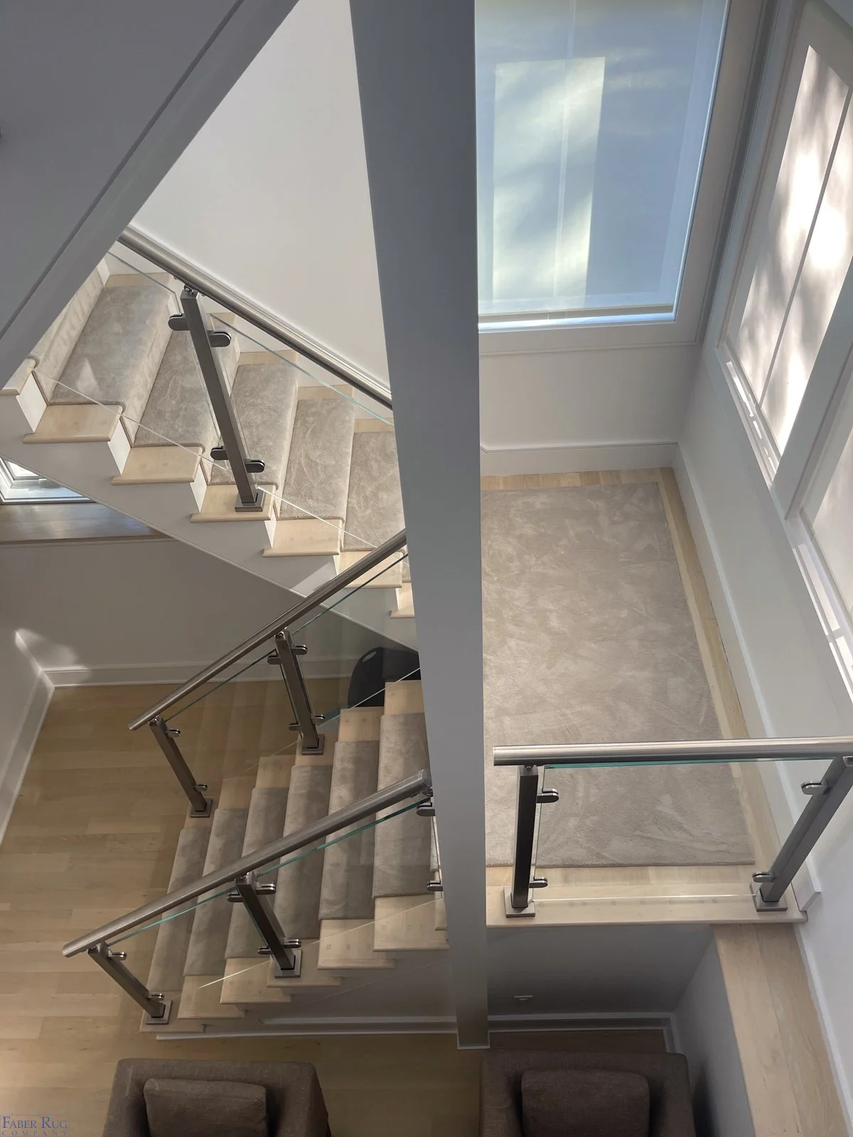 View of a modern staircase with wooden steps, glass and metal railings, leading to an upper level with large windows and a balcony area.