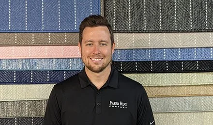 Kyle Faber Smiling in black polo shirt standing in front of a colorful display of carpet samples @faberrug carpet store Wellesley.